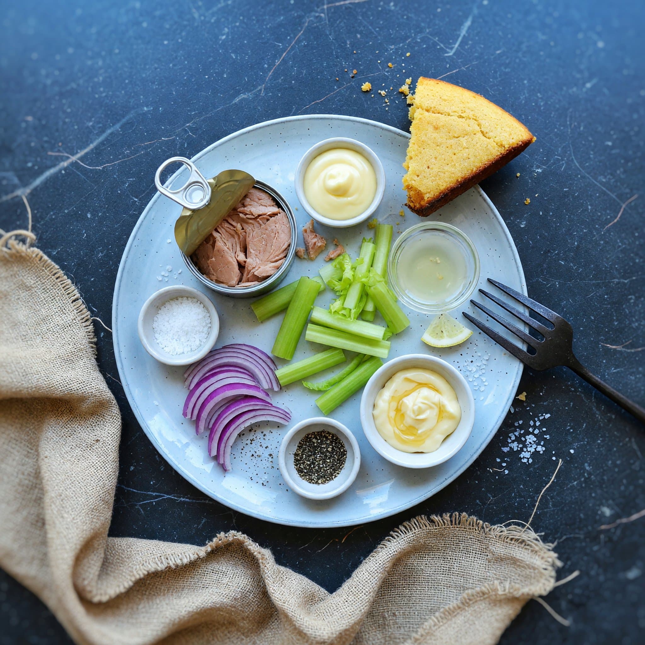 Overhead view of Canned Tuna, Mayonnaise, Celery, Red Onion, Lemon Juice, Salt and Black Pepper arranged on a table